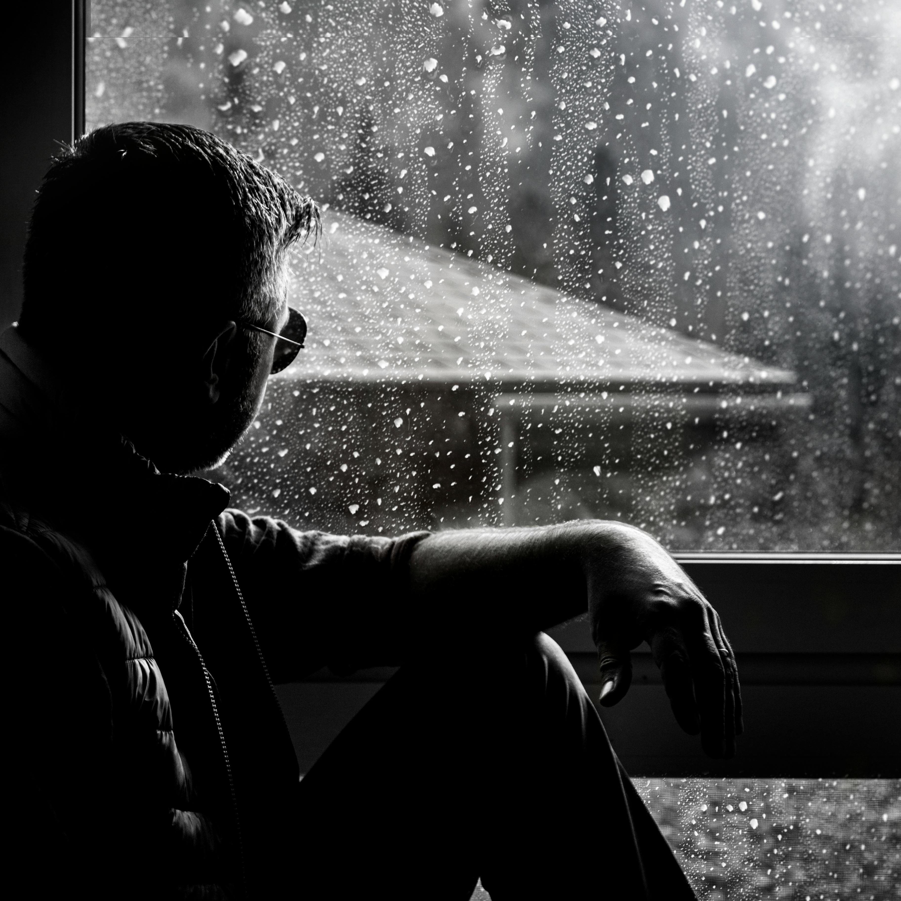 Person sitting by a rain-covered window in silence, expressing introspection, mental overload, and emotional fatigue
